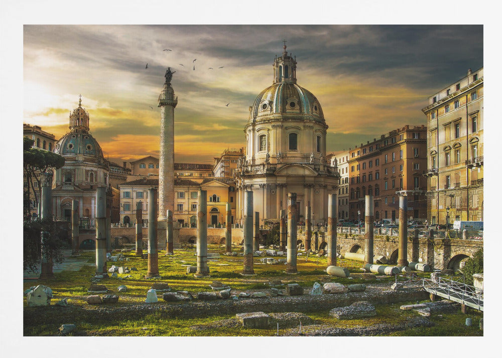 A framed photograph of Trajan's Forum in Rome, Italy, during a dramatic sunset. The foreground is filled with ancient stone columns and ruins on a grassy field, leading to the prominent Trajan's Column and the domed Church of the Most Holy Name of Mary against a golden and dark cloudy sky. Wall Art