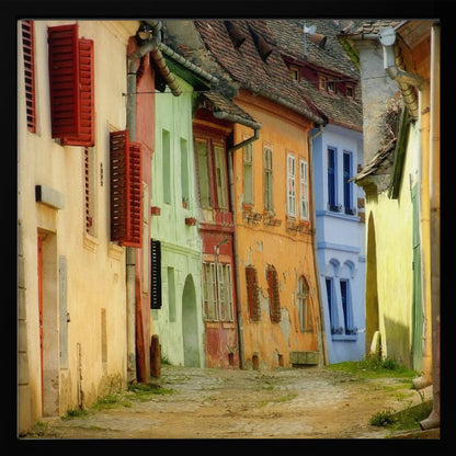 A narrow cobblestone street winds through a historic European town, flanked by colorful, weathered buildings in shades of cream, green, orange, and blue with red shutters, all under aged tile roofs and enclosed in a light wood frame. Artwork
