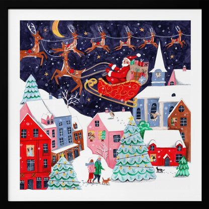 A festive illustration of Santa Claus flying in his sleigh pulled by reindeer over a snowy European-style village at night. The sky is a deep starry blue with a crescent moon, and the houses below are painted in vibrant reds, pinks, and blues, with warm light in the windows. People walk in the snow near decorated Christmas trees. Decor