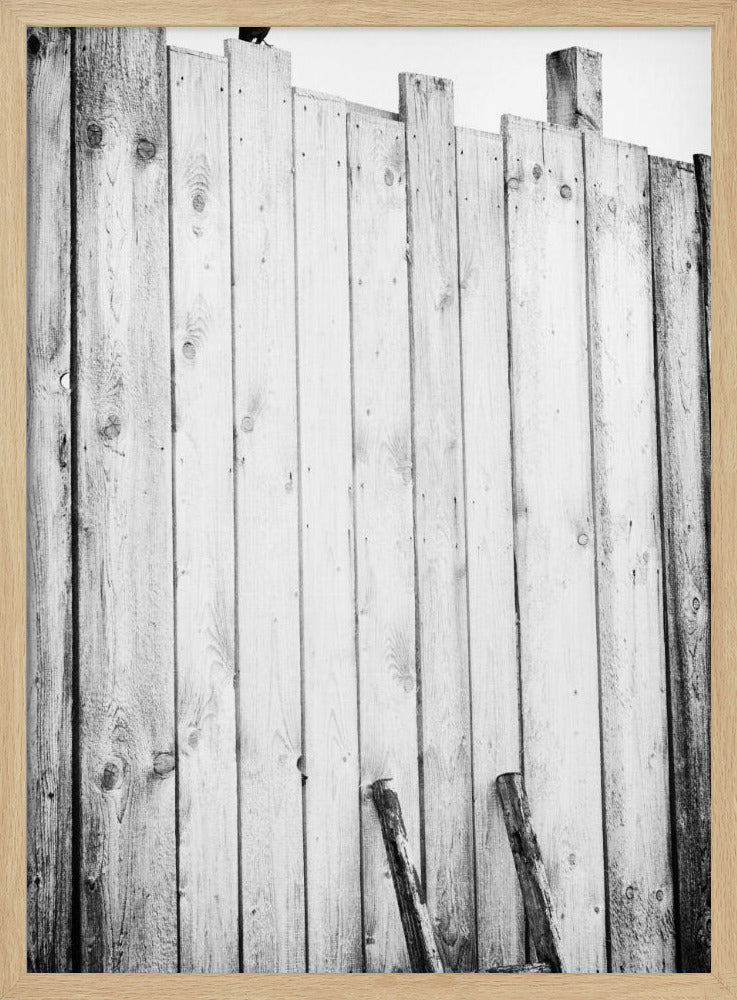 A black and white, low-angle photograph of a weathered wooden plank fence. The vertical planks are of varying heights, creating an uneven top line against a pale sky. The focus is on the texture of the wood, showing prominent grain, knots, and nail holes, all framed in black. Poster