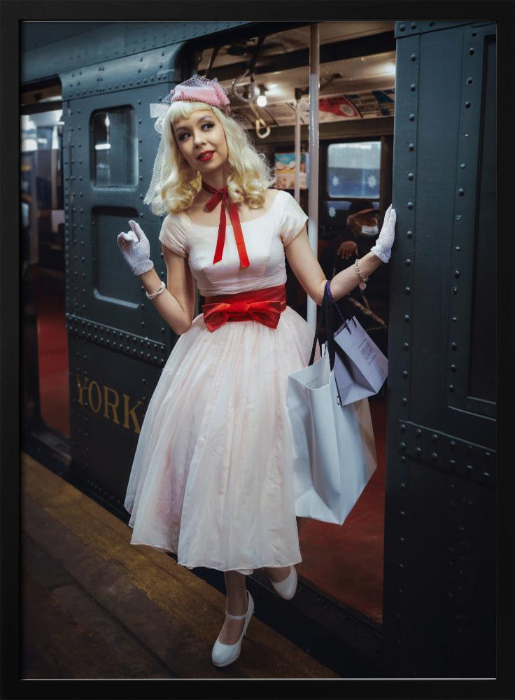 A full-length portrait of a young woman with blonde hair dressed in 1950s-style fashion, including a light pink dress with a bright red sash, a pink veiled hat, and white gloves. She smiles as she steps out of a dark, vintage train car onto a platform, holding shopping bags. Poster