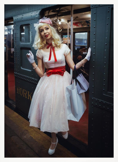 A full-length portrait of a young woman with blonde hair dressed in 1950s-style fashion, including a light pink dress with a bright red sash, a pink veiled hat, and white gloves. She smiles as she steps out of a dark, vintage train car onto a platform, holding shopping bags. Poster
