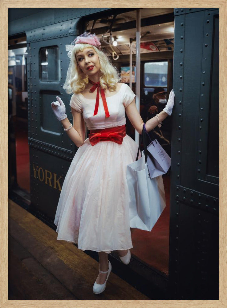 A full-length portrait of a young woman with blonde hair dressed in 1950s-style fashion, including a light pink dress with a bright red sash, a pink veiled hat, and white gloves. She smiles as she steps out of a dark, vintage train car onto a platform, holding shopping bags. Poster