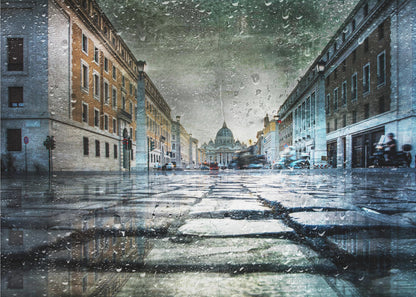 A low-angle, artistic photograph of a wet cobblestone street in Rome leading to St. Peter's Basilica in the distance. The image has a moody, textured feel with an overlay of raindrops, as if viewed through a rainy window, and reflections of the historic buildings in the puddles on the street. Decor