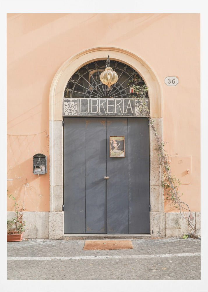 A charming European bookstore entrance featuring a large, dark grey arched door set against a peach-colored wall. Above the door, a sign reads 'LIBRERIA' below a decorative fanlight window and a hanging lantern. Decor