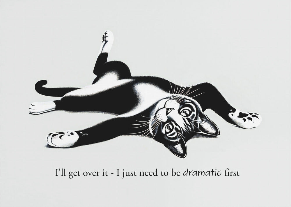 A framed black and white illustration of a tuxedo cat lying playfully on its back. Below the image is the text, 'I'll get over it - I just need to be dramatic first'. Artwork