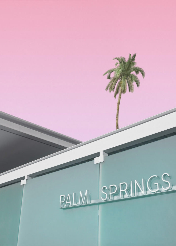 A low-angle shot of a modern building with a frosted teal glass facade and a white neon sign that reads 'PALM SPRINGS'. Above the building, a single tall palm tree stands against a solid, vibrant pink sky, creating a minimalist and stylized composition. Decor