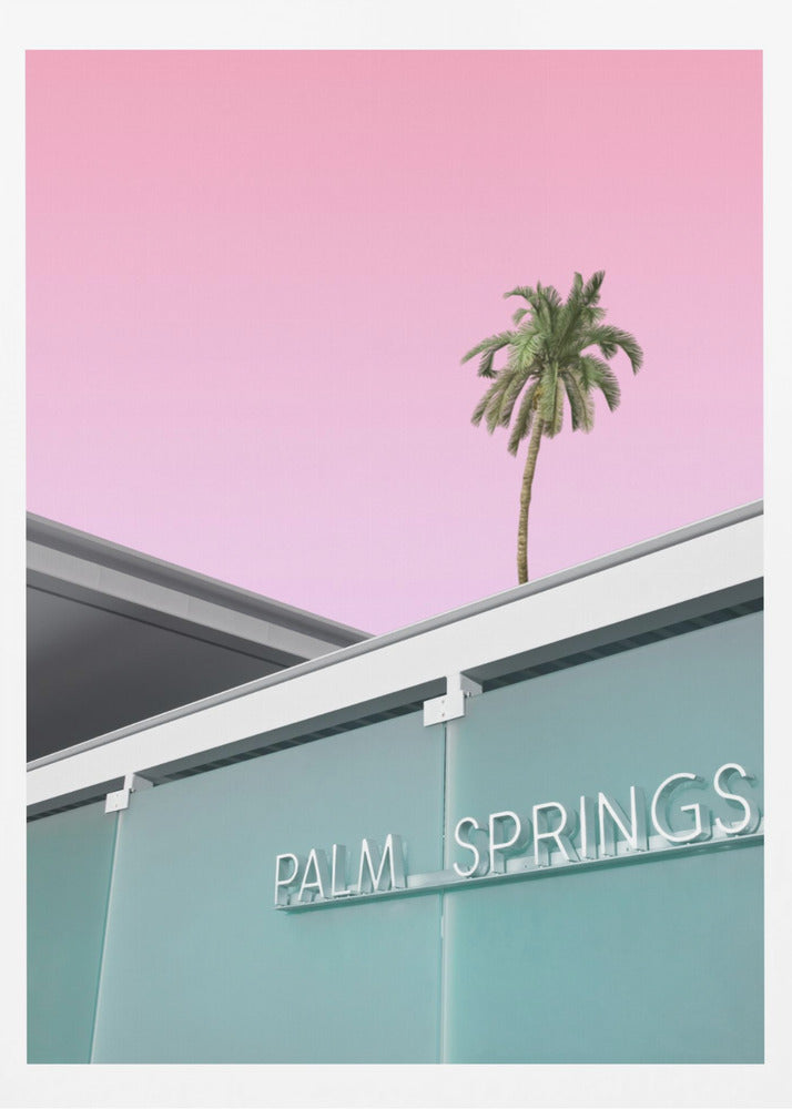 A low-angle shot of a modern building with a frosted teal glass facade and a white neon sign that reads 'PALM SPRINGS'. Above the building, a single tall palm tree stands against a solid, vibrant pink sky, creating a minimalist and stylized composition. Decor