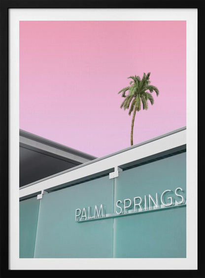 A low-angle shot of a modern building with a frosted teal glass facade and a white neon sign that reads 'PALM SPRINGS'. Above the building, a single tall palm tree stands against a solid, vibrant pink sky, creating a minimalist and stylized composition. Decor