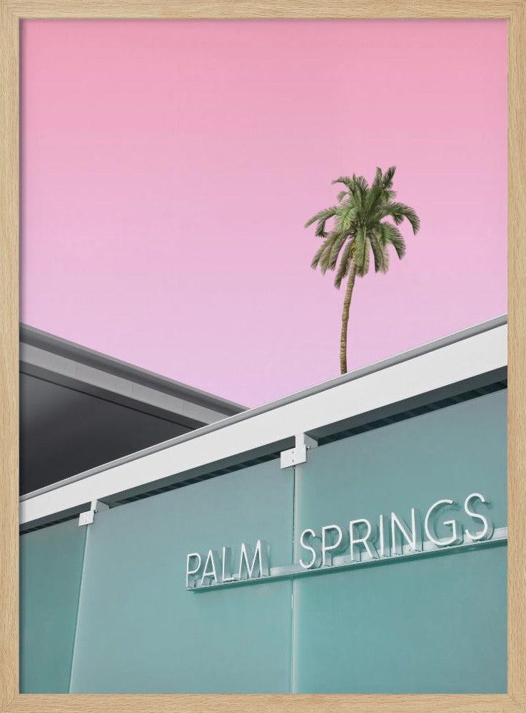 A low-angle shot of a modern building with a frosted teal glass facade and a white neon sign that reads 'PALM SPRINGS'. Above the building, a single tall palm tree stands against a solid, vibrant pink sky, creating a minimalist and stylized composition. Decor