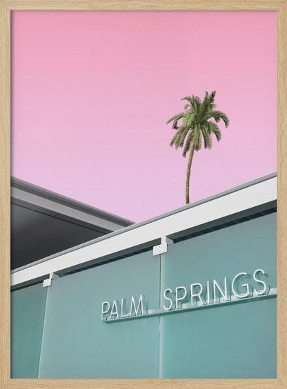 A low-angle shot of a modern building with a frosted teal glass facade and a white neon sign that reads 'PALM SPRINGS'. Above the building, a single tall palm tree stands against a solid, vibrant pink sky, creating a minimalist and stylized composition. Decor