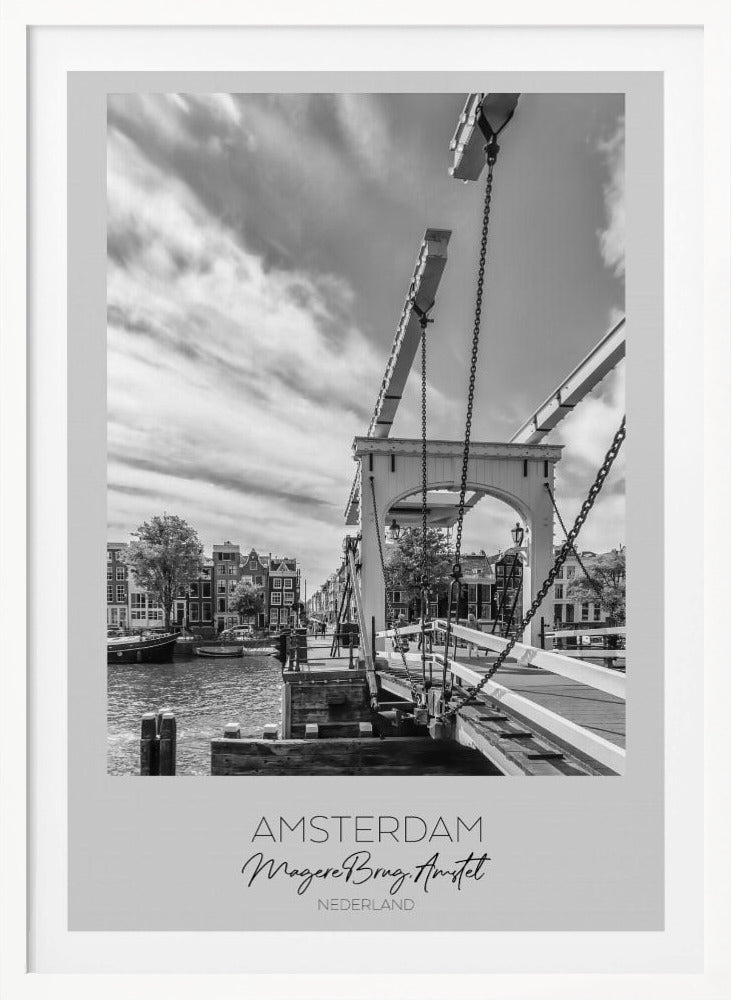 A black and white travel poster of Amsterdam, featuring a side view of the Magere Brug, a traditional wooden drawbridge, over the Amstel river. Classic canal houses line the waterway in the background under a dramatic, cloudy sky. The image is in a black frame and has text at the bottom that reads 'AMSTERDAM', 'Magere Brug, Amstel', and 'NEDERLAND'. Artwork