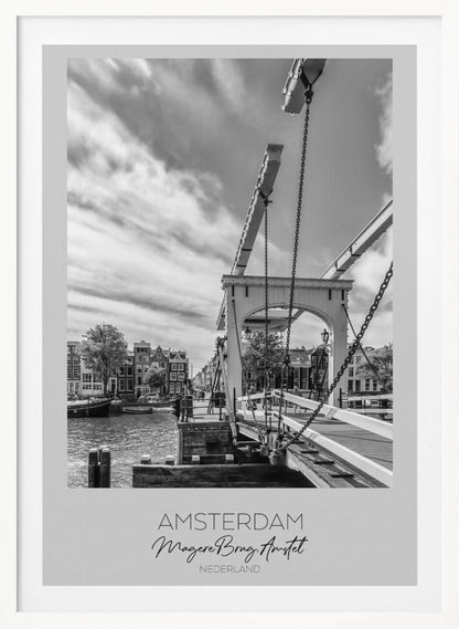A black and white travel poster of Amsterdam, featuring a side view of the Magere Brug, a traditional wooden drawbridge, over the Amstel river. Classic canal houses line the waterway in the background under a dramatic, cloudy sky. The image is in a black frame and has text at the bottom that reads 'AMSTERDAM', 'Magere Brug, Amstel', and 'NEDERLAND'. Artwork