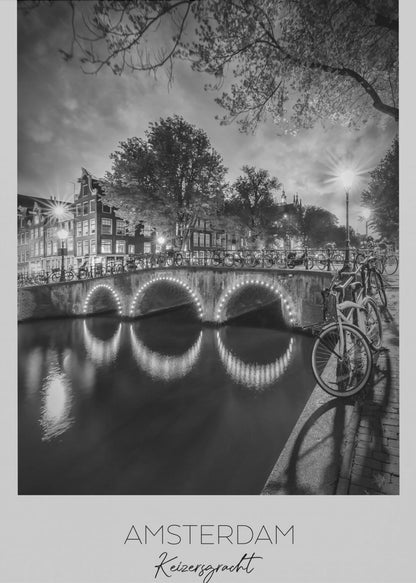A black and white poster of Amsterdam's Keizersgracht canal at night. An arched bridge with glowing lights is the centerpiece, its reflection shimmering on the dark water. Bicycles are parked along the bridge and in the foreground on a cobblestone path. Classic canal houses and trees line the background under a dramatic, cloudy sky. The image is framed with text below reading 'AMSTERDAM Keizersgracht NEDERLAND'. Artwork