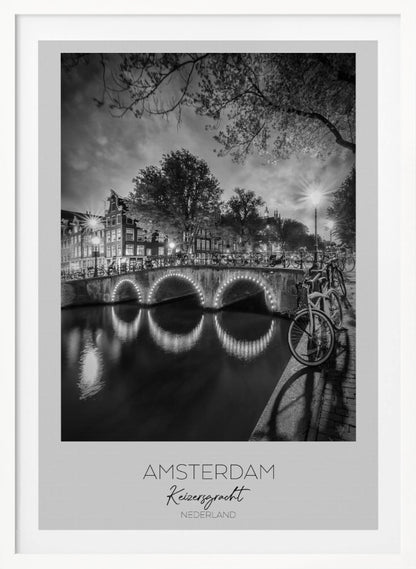 A black and white poster of Amsterdam's Keizersgracht canal at night. An arched bridge with glowing lights is the centerpiece, its reflection shimmering on the dark water. Bicycles are parked along the bridge and in the foreground on a cobblestone path. Classic canal houses and trees line the background under a dramatic, cloudy sky. The image is framed with text below reading 'AMSTERDAM Keizersgracht NEDERLAND'. Artwork