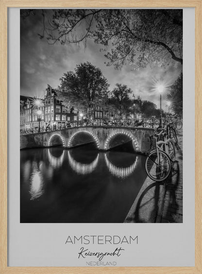 A black and white poster of Amsterdam's Keizersgracht canal at night. An arched bridge with glowing lights is the centerpiece, its reflection shimmering on the dark water. Bicycles are parked along the bridge and in the foreground on a cobblestone path. Classic canal houses and trees line the background under a dramatic, cloudy sky. The image is framed with text below reading 'AMSTERDAM Keizersgracht NEDERLAND'. Artwork