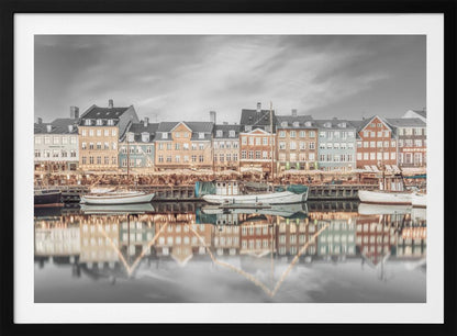 A framed, color-selective photograph of the Nyhavn harbor in Copenhagen. A row of colorful 17th and 18th-century townhouses lines the waterfront, with their warm lights and facades reflecting in the calm canal. The sky and parts of the water are in black and white, making the colored buildings stand out. Several boats are moored along the quay. Decor