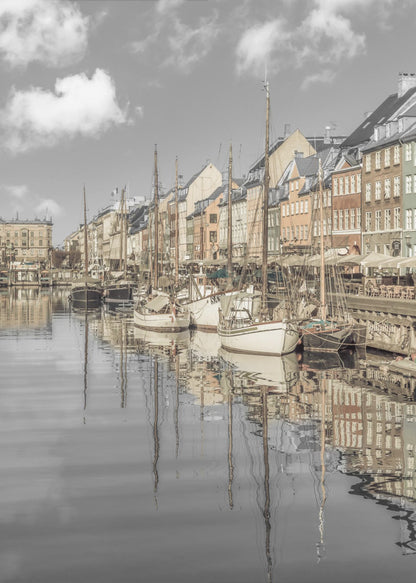 A muted, desaturated photograph of the Nyhavn harbor in Copenhagen. Old-fashioned sailboats are moored along the canal in front of a row of colorful historic buildings. The boats, buildings, and a cloudy sky are perfectly reflected in the calm water. Wall Art