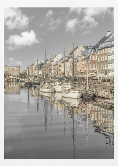 A muted, desaturated photograph of the Nyhavn harbor in Copenhagen. Old-fashioned sailboats are moored along the canal in front of a row of colorful historic buildings. The boats, buildings, and a cloudy sky are perfectly reflected in the calm water. Wall Art