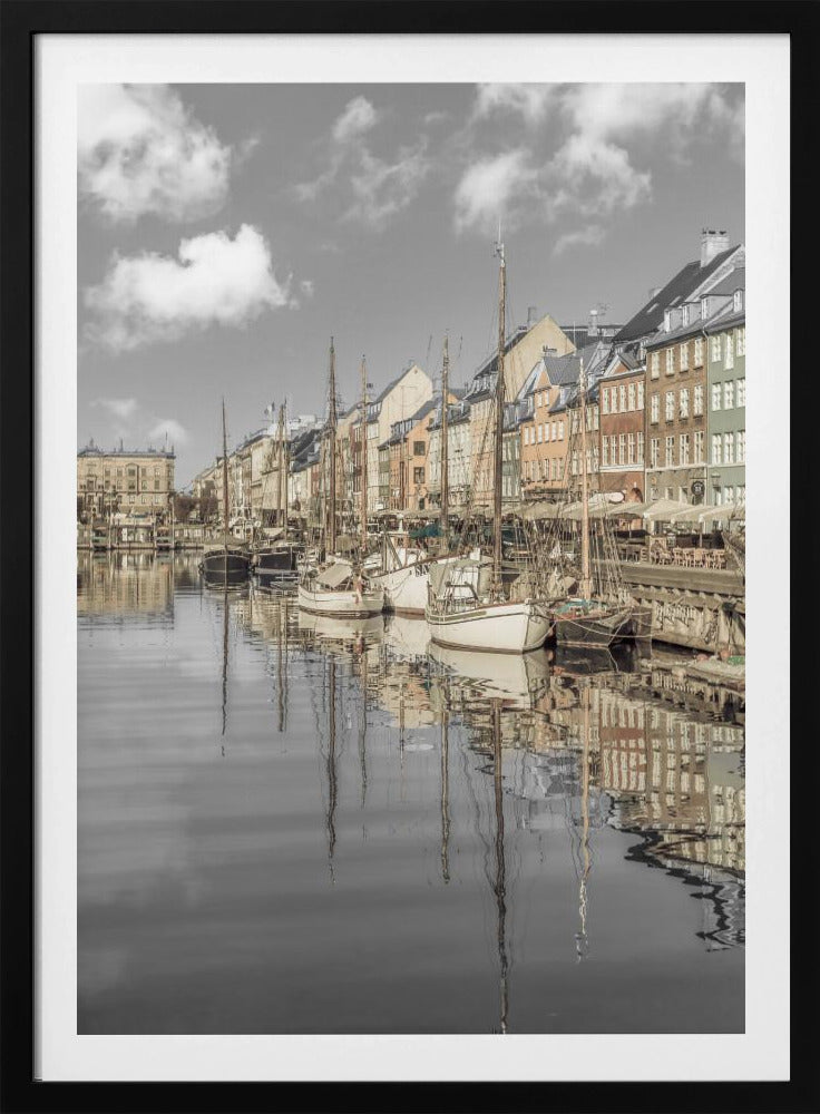 A muted, desaturated photograph of the Nyhavn harbor in Copenhagen. Old-fashioned sailboats are moored along the canal in front of a row of colorful historic buildings. The boats, buildings, and a cloudy sky are perfectly reflected in the calm water. Wall Art