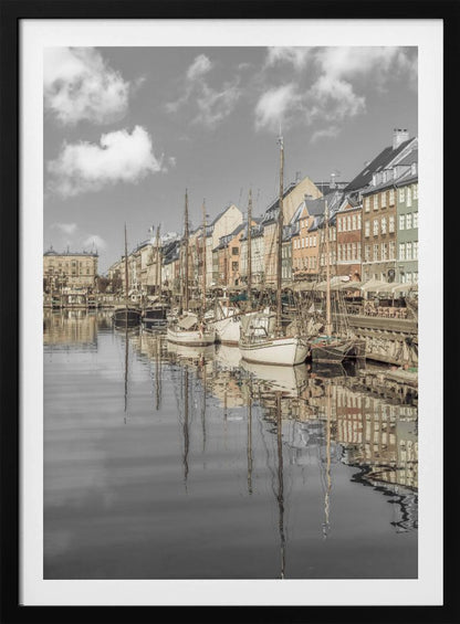A muted, desaturated photograph of the Nyhavn harbor in Copenhagen. Old-fashioned sailboats are moored along the canal in front of a row of colorful historic buildings. The boats, buildings, and a cloudy sky are perfectly reflected in the calm water. Wall Art