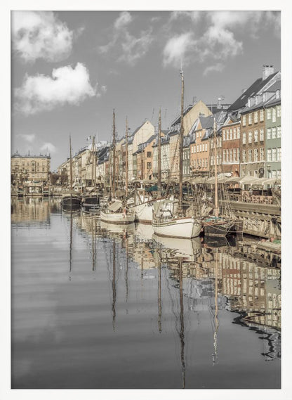 A muted, desaturated photograph of the Nyhavn harbor in Copenhagen. Old-fashioned sailboats are moored along the canal in front of a row of colorful historic buildings. The boats, buildings, and a cloudy sky are perfectly reflected in the calm water. Wall Art