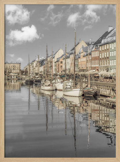 A muted, desaturated photograph of the Nyhavn harbor in Copenhagen. Old-fashioned sailboats are moored along the canal in front of a row of colorful historic buildings. The boats, buildings, and a cloudy sky are perfectly reflected in the calm water. Wall Art