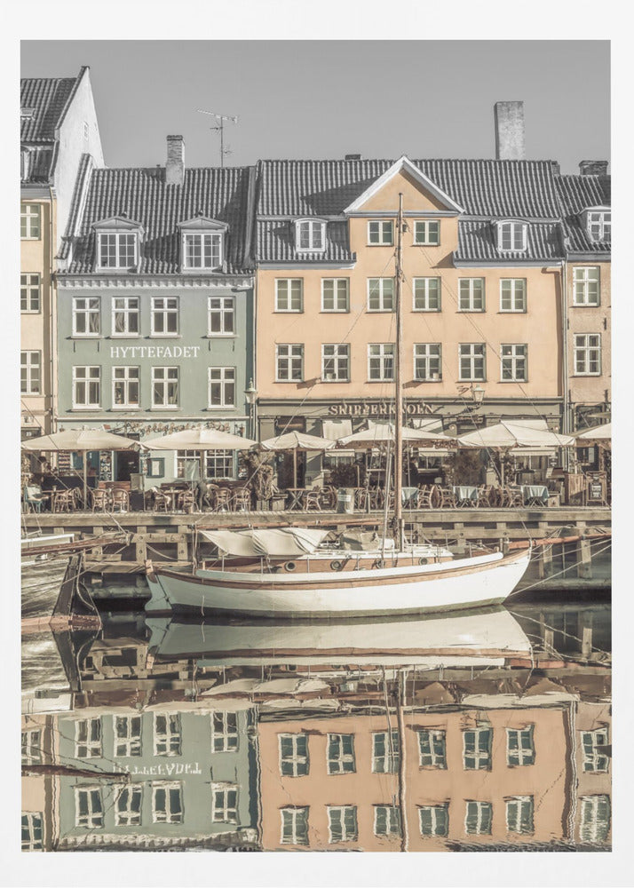 A scenic photograph of a European harbor with colorful buildings reflected in the water. A white sailboat is moored in the foreground in front of a pale green and a yellow gabled building. The image has a selective color effect, with the building facades in muted tones and the sky and roofs in black and white. Artwork