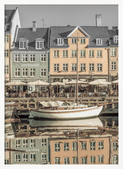 A scenic photograph of a European harbor with colorful buildings reflected in the water. A white sailboat is moored in the foreground in front of a pale green and a yellow gabled building. The image has a selective color effect, with the building facades in muted tones and the sky and roofs in black and white. Artwork