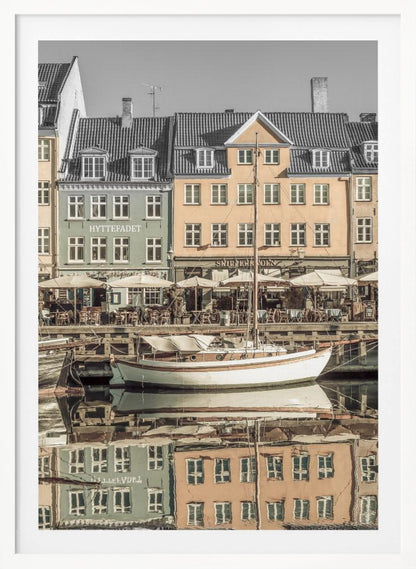 A scenic photograph of a European harbor with colorful buildings reflected in the water. A white sailboat is moored in the foreground in front of a pale green and a yellow gabled building. The image has a selective color effect, with the building facades in muted tones and the sky and roofs in black and white. Artwork