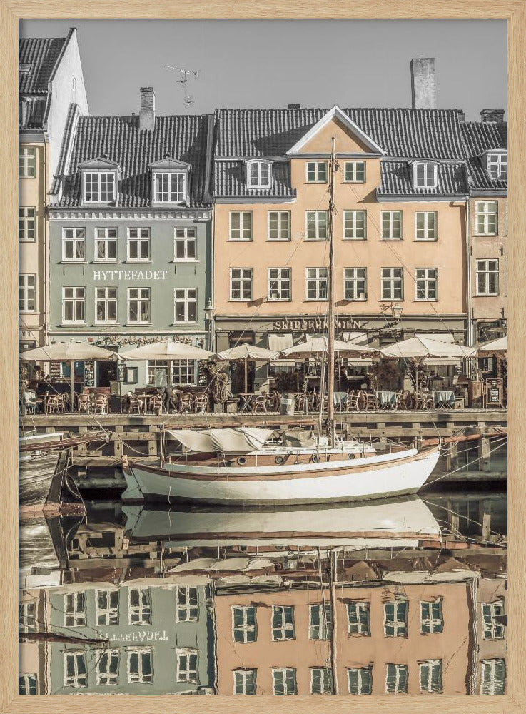 A scenic photograph of a European harbor with colorful buildings reflected in the water. A white sailboat is moored in the foreground in front of a pale green and a yellow gabled building. The image has a selective color effect, with the building facades in muted tones and the sky and roofs in black and white. Artwork