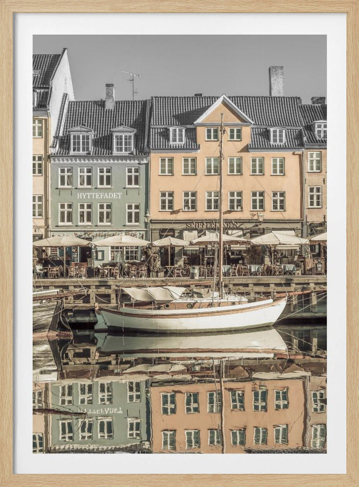 A scenic photograph of a European harbor with colorful buildings reflected in the water. A white sailboat is moored in the foreground in front of a pale green and a yellow gabled building. The image has a selective color effect, with the building facades in muted tones and the sky and roofs in black and white. Artwork
