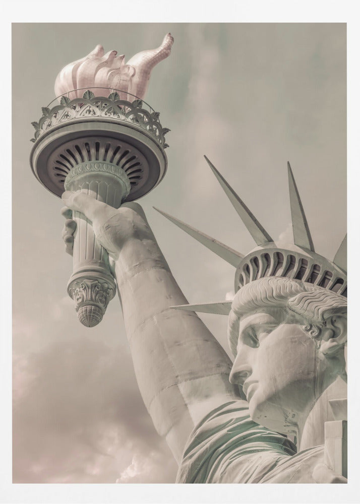A low-angle, close-up photograph of the Statue of Liberty with a vintage color treatment. The shot captures her profile, crown, and her arm holding the torch aloft against a muted, cloudy sky, all enclosed in a thin black frame. Poster