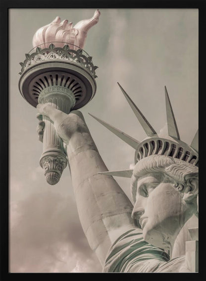 A low-angle, close-up photograph of the Statue of Liberty with a vintage color treatment. The shot captures her profile, crown, and her arm holding the torch aloft against a muted, cloudy sky, all enclosed in a thin black frame. Poster