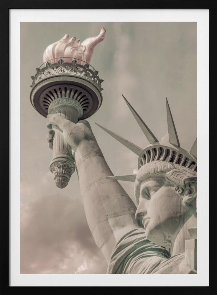 A low-angle, close-up photograph of the Statue of Liberty with a vintage color treatment. The shot captures her profile, crown, and her arm holding the torch aloft against a muted, cloudy sky, all enclosed in a thin black frame. Poster