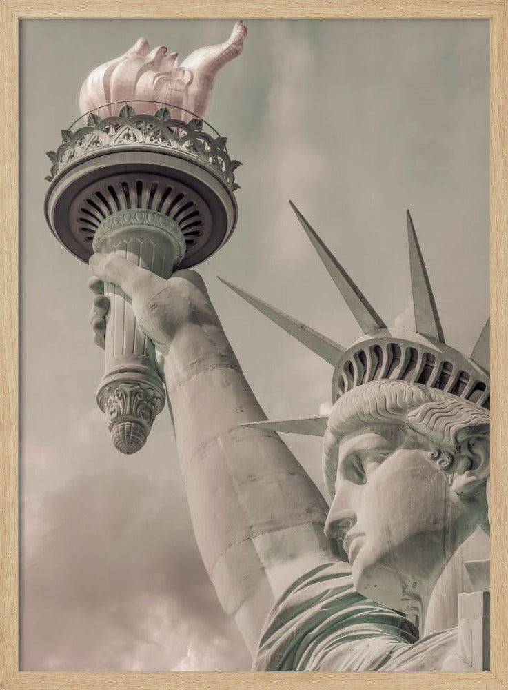 A low-angle, close-up photograph of the Statue of Liberty with a vintage color treatment. The shot captures her profile, crown, and her arm holding the torch aloft against a muted, cloudy sky, all enclosed in a thin black frame. Poster
