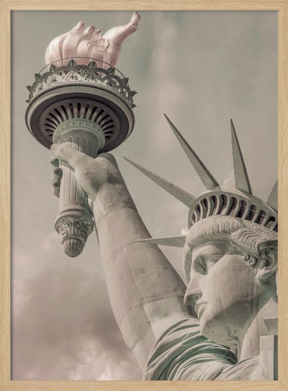 A low-angle, close-up photograph of the Statue of Liberty with a vintage color treatment. The shot captures her profile, crown, and her arm holding the torch aloft against a muted, cloudy sky, all enclosed in a thin black frame. Poster