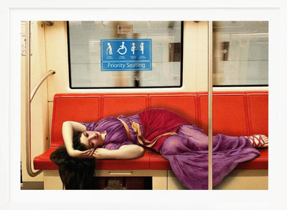 A framed surrealist artwork depicting a woman in a classical purple and red toga sleeping across a row of modern red subway seats. Above her on the window is a blue 'Priority Seating' sign, creating a humorous juxtaposition between ancient and modern life. Artwork