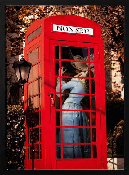A couple in vintage clothing share a passionate kiss inside a classic bright red telephone booth. The woman is wearing a light blue dress, and the man wears a hat. The sign above the booth door reads 'NON STOP'. The setting appears to be outdoors in autumn. Wall Art