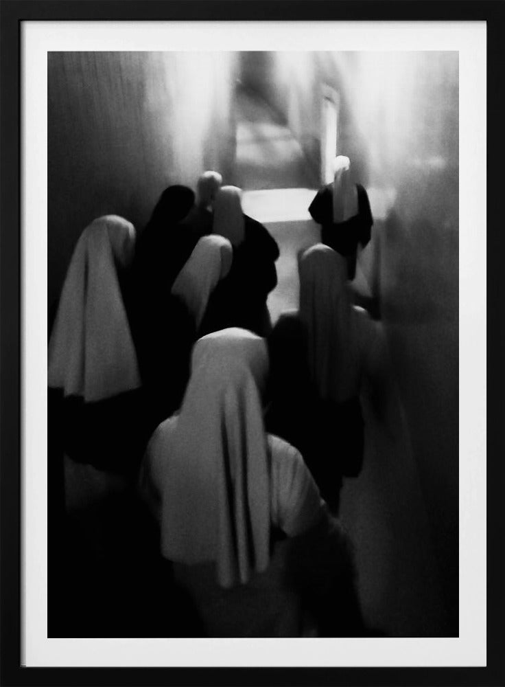 A mysterious black and white photograph captures a group of robed figures, possibly nuns, from above as they walk down a dark, narrow corridor. The image is blurred, creating a ghostly, ethereal atmosphere as the figures' white head coverings stand out against the deep shadows. Artwork