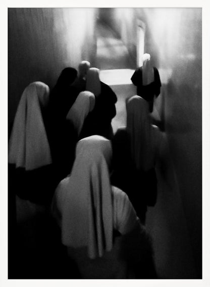 A mysterious black and white photograph captures a group of robed figures, possibly nuns, from above as they walk down a dark, narrow corridor. The image is blurred, creating a ghostly, ethereal atmosphere as the figures' white head coverings stand out against the deep shadows. Artwork