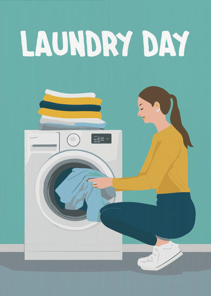 A framed illustration poster with the words 'LAUNDRY DAY' in white at the top. A woman with brown hair in a ponytail, wearing a yellow top and blue pants, crouches to load blue clothes into a white front-loading washing machine. A stack of folded laundry sits atop the machine against a teal background. Print