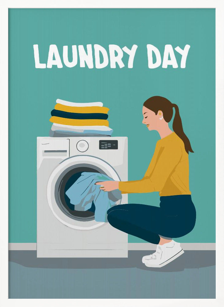 A framed illustration poster with the words 'LAUNDRY DAY' in white at the top. A woman with brown hair in a ponytail, wearing a yellow top and blue pants, crouches to load blue clothes into a white front-loading washing machine. A stack of folded laundry sits atop the machine against a teal background. Print