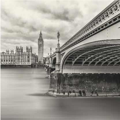A framed, long-exposure, black and white photograph of London. The image shows Westminster Bridge from a low angle on the right, with the River Thames appearing smooth and misty. In the background on the left are the Houses of Parliament and the Big Ben clock tower under a cloudy sky. Wall Art