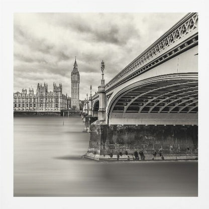 A framed, long-exposure, black and white photograph of London. The image shows Westminster Bridge from a low angle on the right, with the River Thames appearing smooth and misty. In the background on the left are the Houses of Parliament and the Big Ben clock tower under a cloudy sky. Wall Art