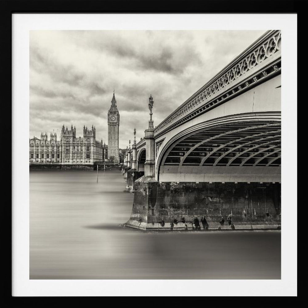A framed, long-exposure, black and white photograph of London. The image shows Westminster Bridge from a low angle on the right, with the River Thames appearing smooth and misty. In the background on the left are the Houses of Parliament and the Big Ben clock tower under a cloudy sky. Wall Art