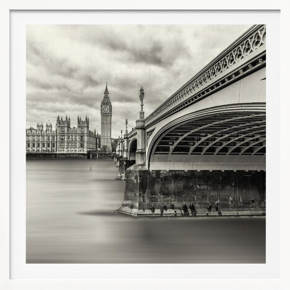 A framed, long-exposure, black and white photograph of London. The image shows Westminster Bridge from a low angle on the right, with the River Thames appearing smooth and misty. In the background on the left are the Houses of Parliament and the Big Ben clock tower under a cloudy sky. Wall Art