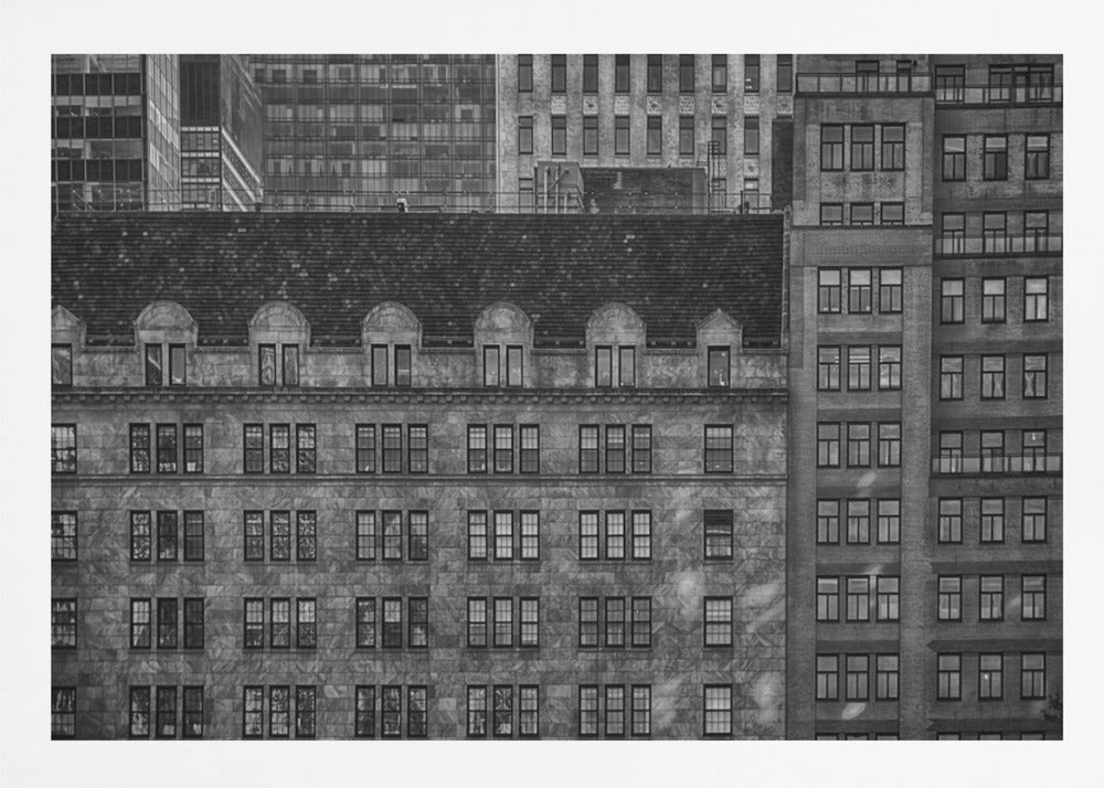 A dense, black and white photograph of various city buildings packed closely together. The image highlights the contrasting architectural styles, from an older stone building with a dark roof in the foreground to taller brick and modern glass buildings in the background, creating a geometric pattern of windows and textures. Decor