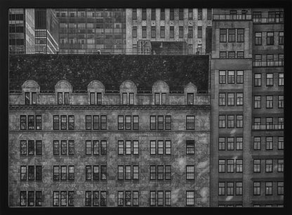 A dense, black and white photograph of various city buildings packed closely together. The image highlights the contrasting architectural styles, from an older stone building with a dark roof in the foreground to taller brick and modern glass buildings in the background, creating a geometric pattern of windows and textures. Decor
