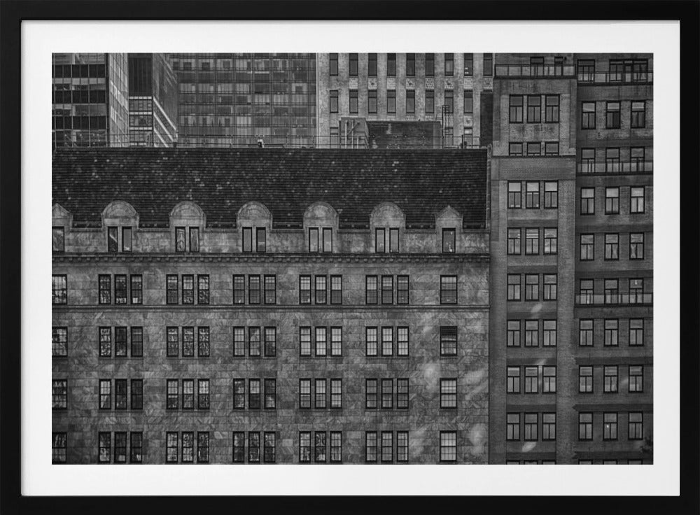 A dense, black and white photograph of various city buildings packed closely together. The image highlights the contrasting architectural styles, from an older stone building with a dark roof in the foreground to taller brick and modern glass buildings in the background, creating a geometric pattern of windows and textures. Decor